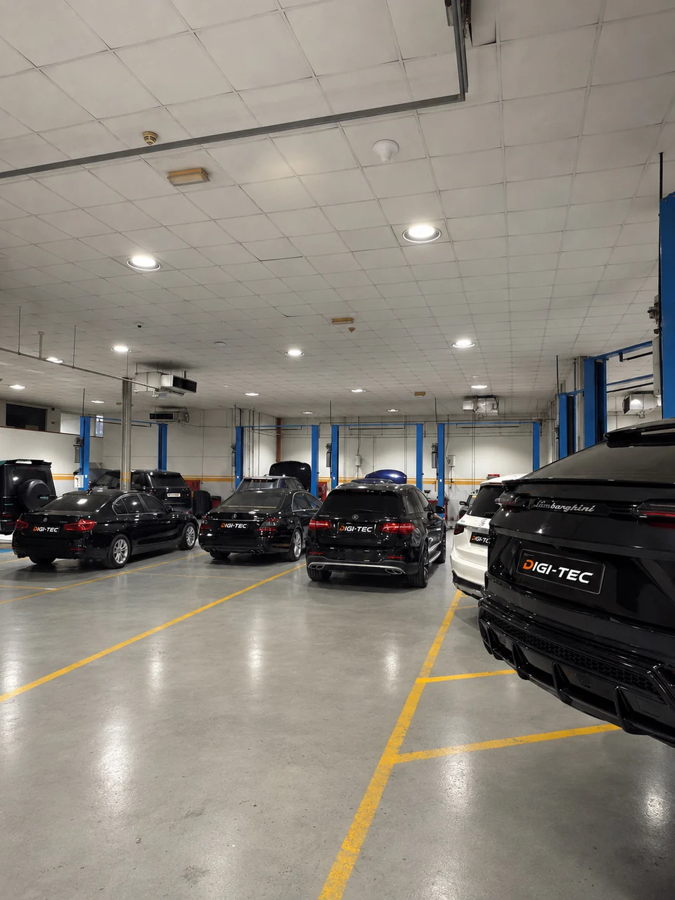 Luxury vehicles with DIGI-TEC plates parked in the workshop, including a Lamborghini SUV